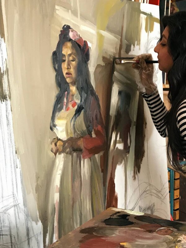 A woman in a striped top painting a portrait in oil paint.